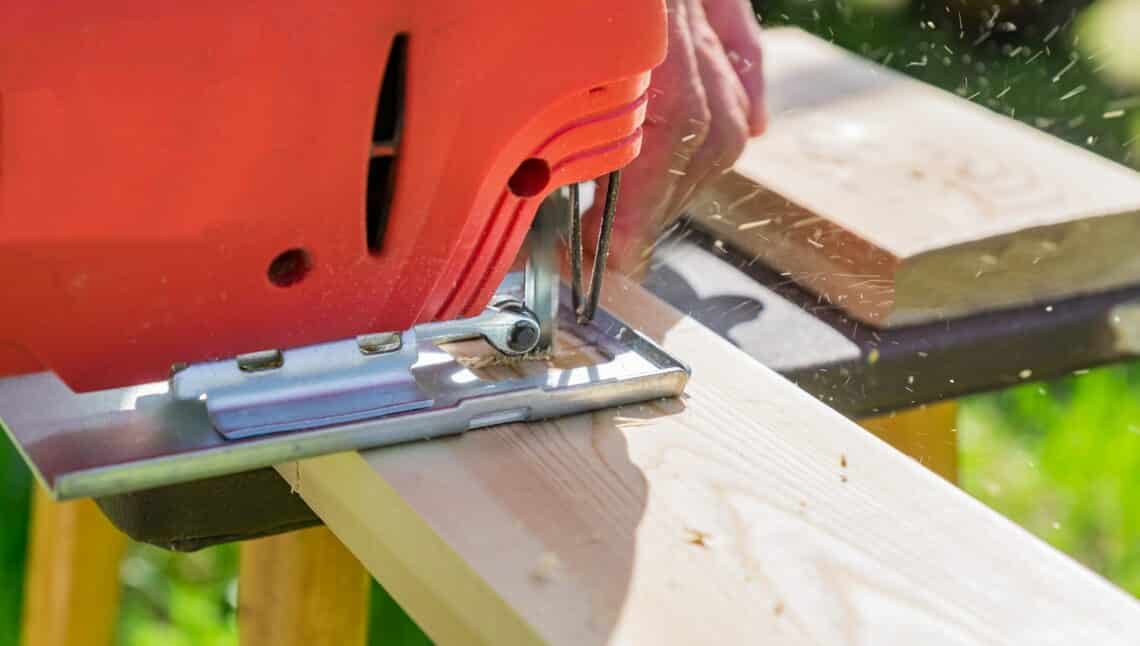 wood worker cutting wooden panel with jig saw outdoors, Close-up view of man working with electric jigsaw and wooden plank